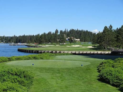 Manicured green framed by tall pines with Lake Coeur d'Alene beyond